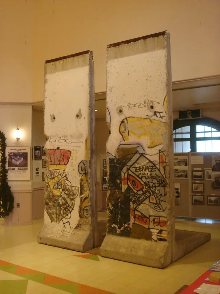 Two graffitied Berlin Wall elements standing side by side on a display floor inside a museum hall.
