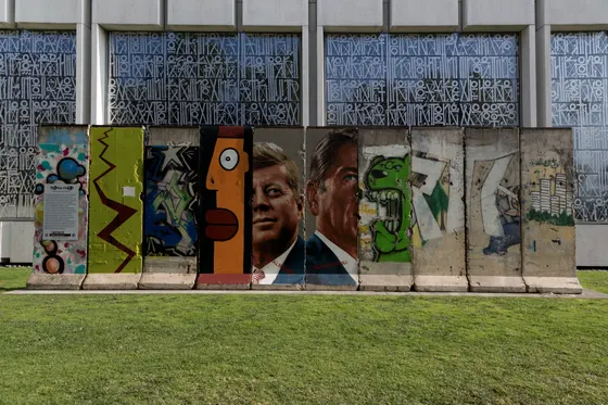 A long run of painted Berlin Wall segments along a boulevard in Los Angeles.