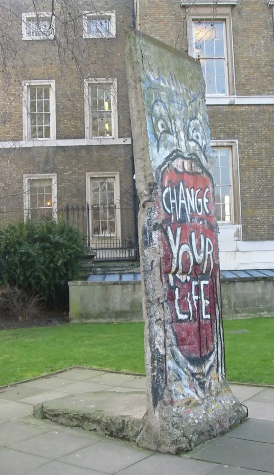 A Berlin Wall segment painted with an open red mouth reading CHANGE YOUR LIFE, standing in a park.