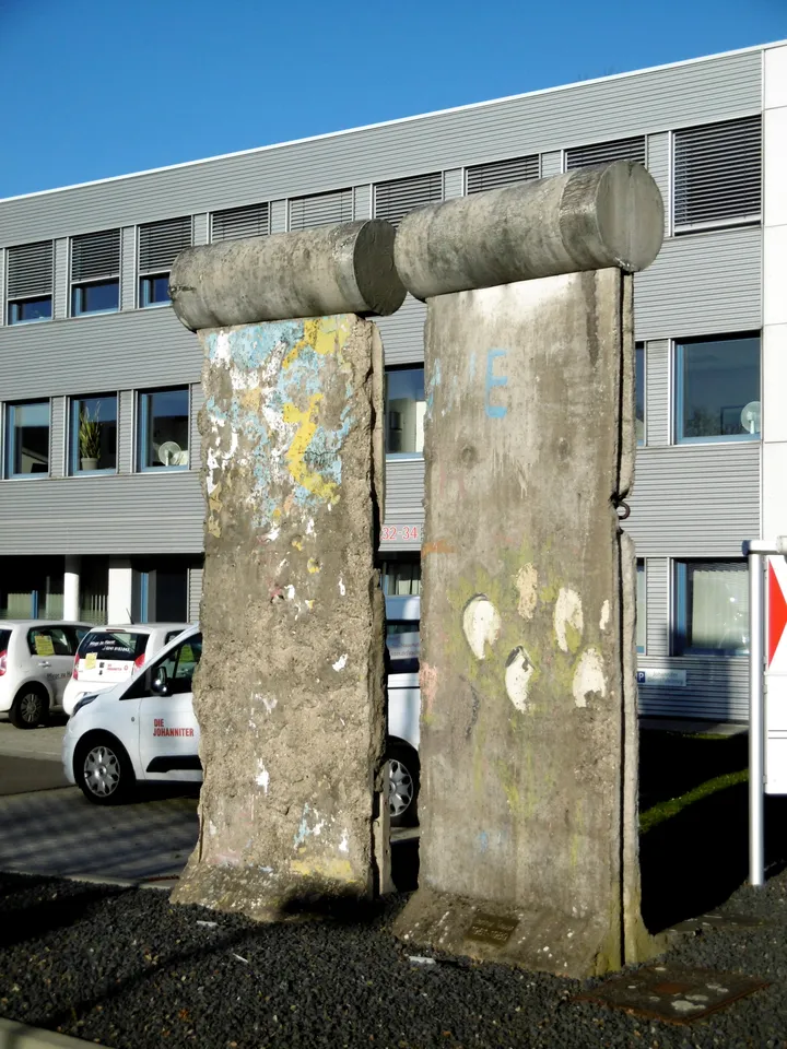 Painted Berlin Wall elements standing on grass in front of a modern building.