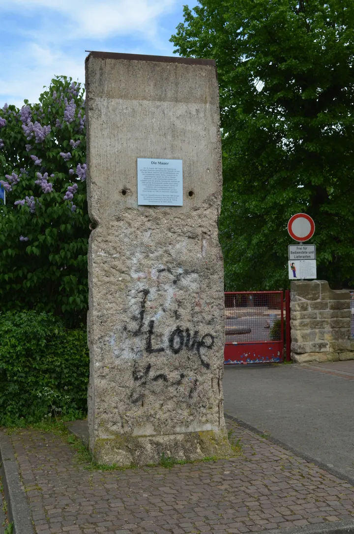 A concrete Berlin Wall element standing beside a building on a town street.