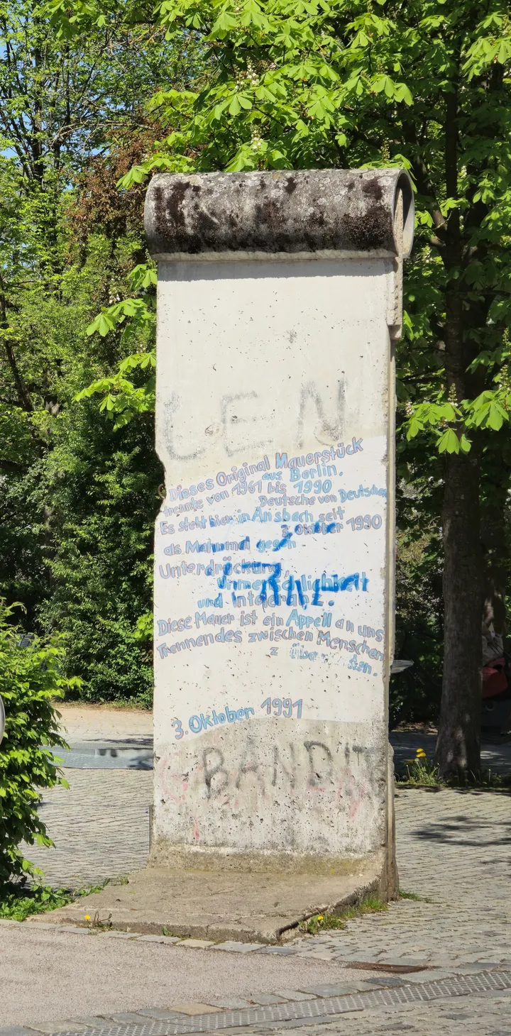 A tall painted Berlin Wall element standing outdoors among trees.