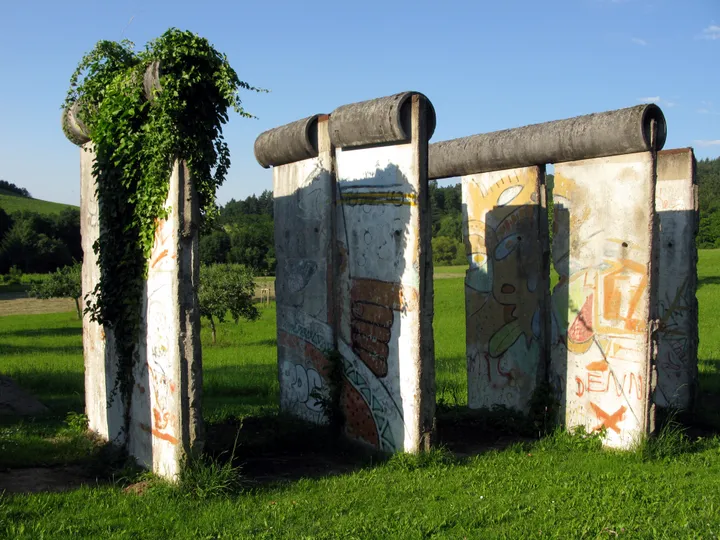 Sections of the Berlin Wall standing beside a road in a rural village with hills behind.