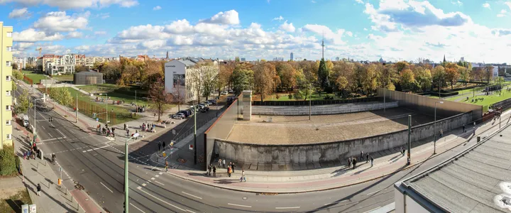 A preserved run of the Berlin Wall with the raked border strip and rows of marker poles behind it.