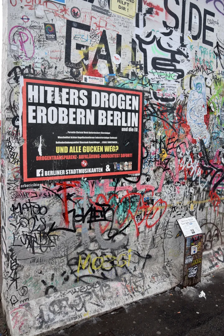 A long painted run of the Berlin Wall beside a pavement, covered in murals.