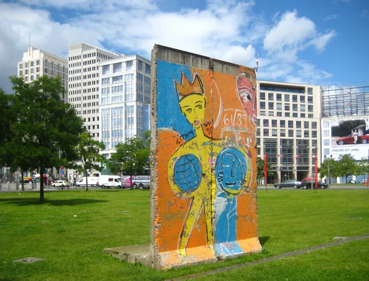 A short run of Berlin Wall segments standing against a brick fire wall beside a pavement.