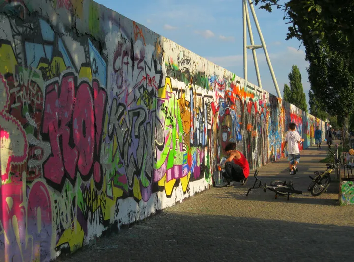 A graffiti-covered concrete wall running along the edge of a park on a slope.