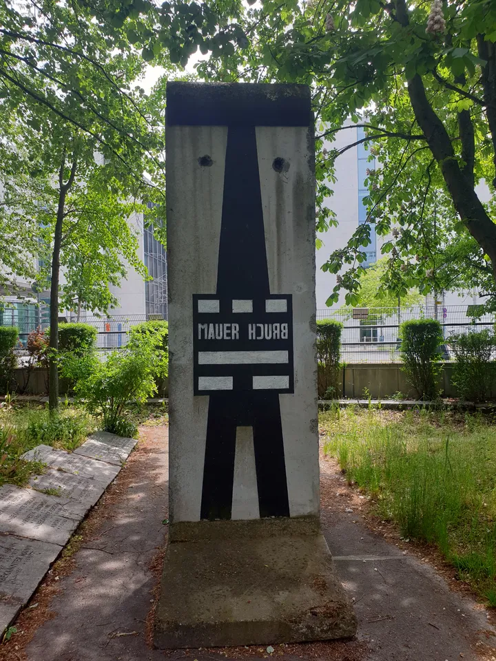 A painted Berlin Wall element standing among trees and planting beside a path.