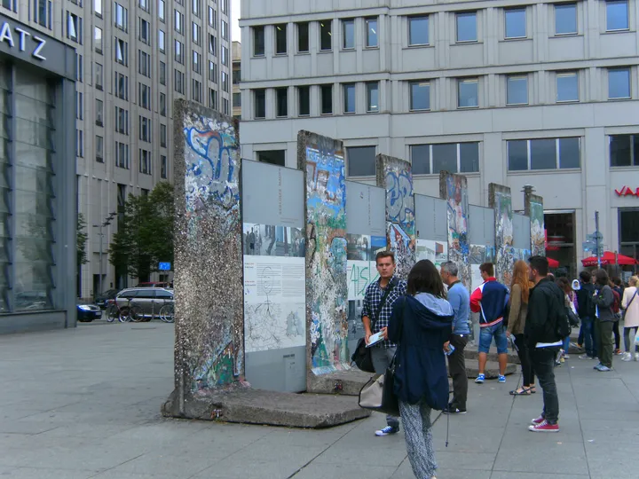 A row of graffitied Berlin Wall segments standing in a paved city square.