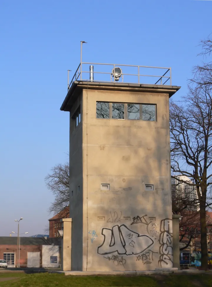 A square four-storey concrete watchtower with large windows on the top floor, standing among trees.
