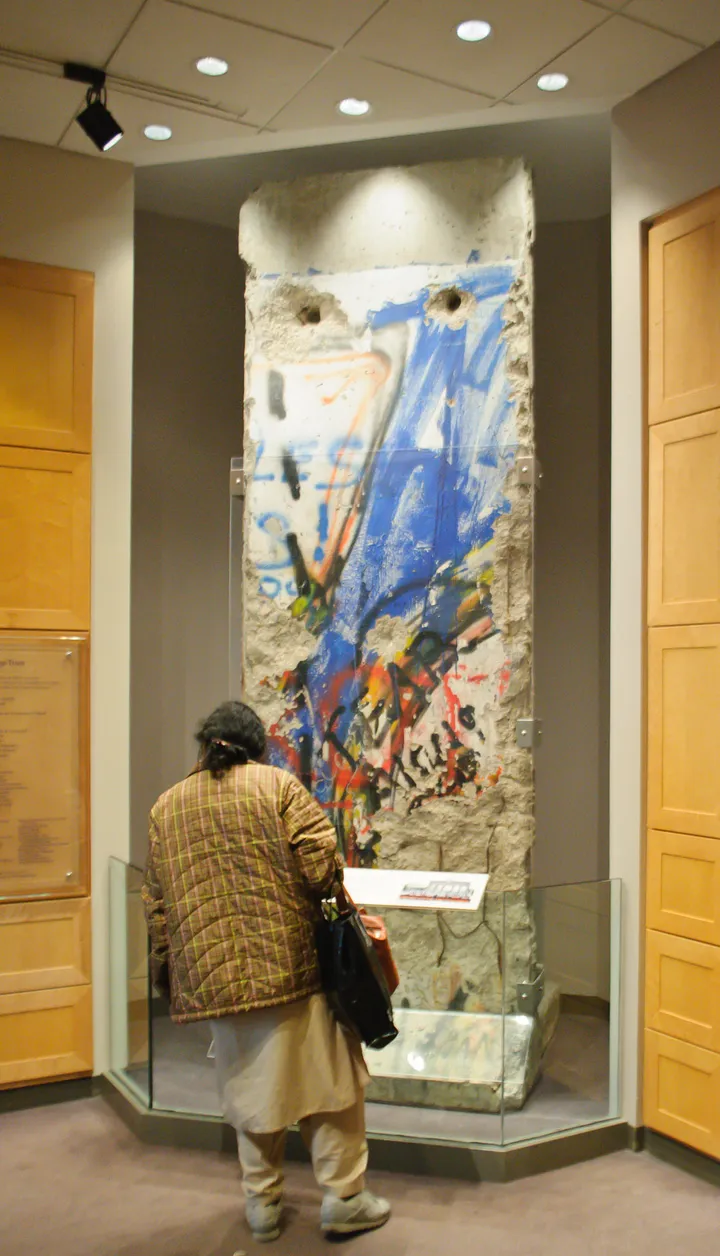 A painted section of the Berlin Wall displayed indoors beside a window wall.