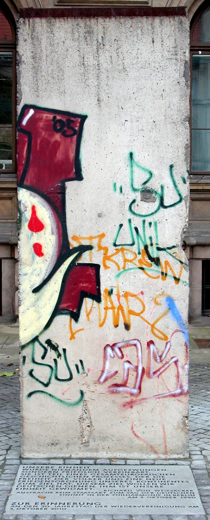 A tall concrete wall element standing as a memorial with a plaque at its base.