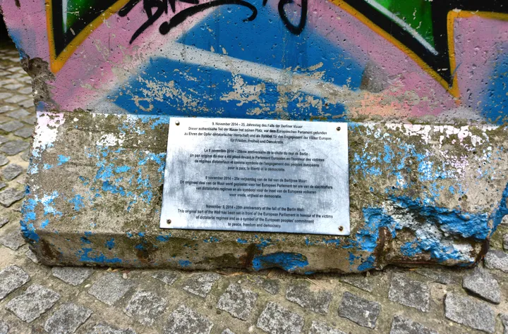 A painted Berlin Wall segment on a plinth outside a large modern glass building.