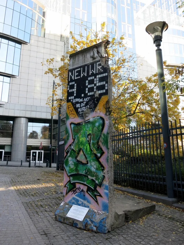 A painted Berlin Wall section standing on a pavement near a large institutional building.