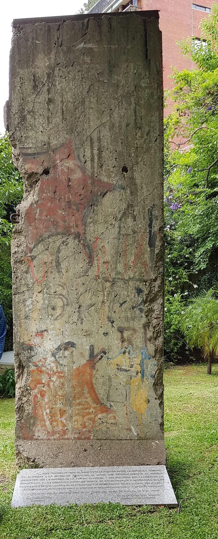 A tall painted Berlin Wall segment standing in a courtyard garden.
