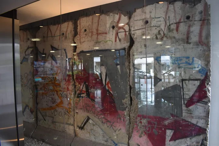 A painted Berlin Wall segment standing outdoors beside a modern office building.