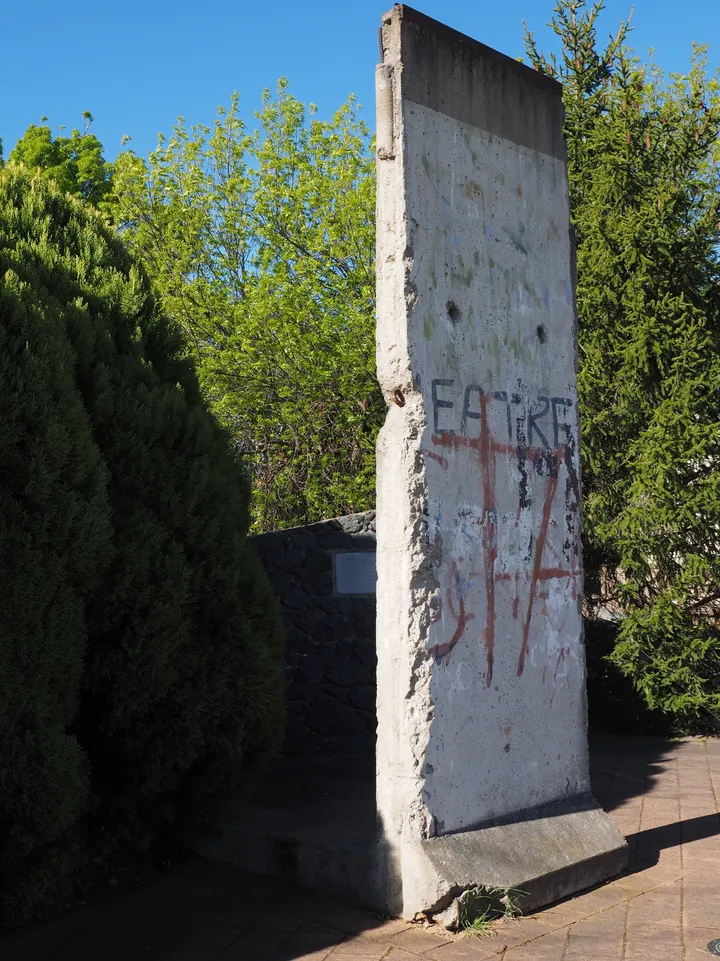 A painted Berlin Wall section mounted outdoors in front of a low brick clubhouse.