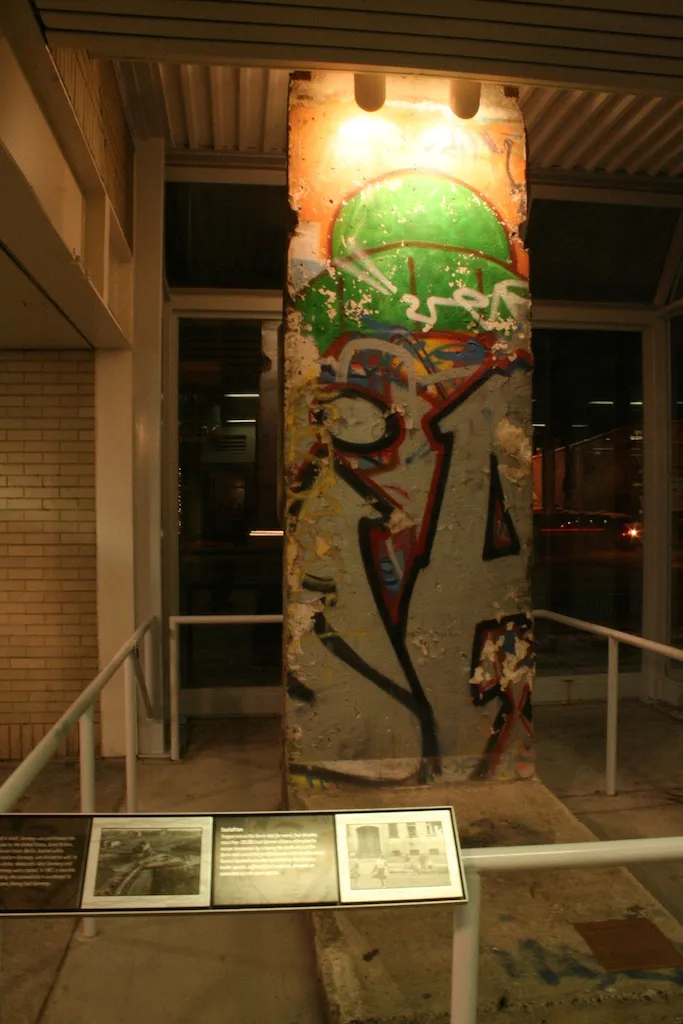 A painted Berlin Wall segment standing inside a lit railway station at night.
