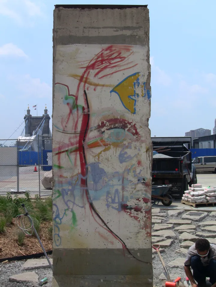 A painted Berlin Wall section standing on a paved plaza outside a modern building.