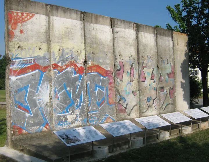 A run of painted Berlin Wall segments standing outdoors on grass.