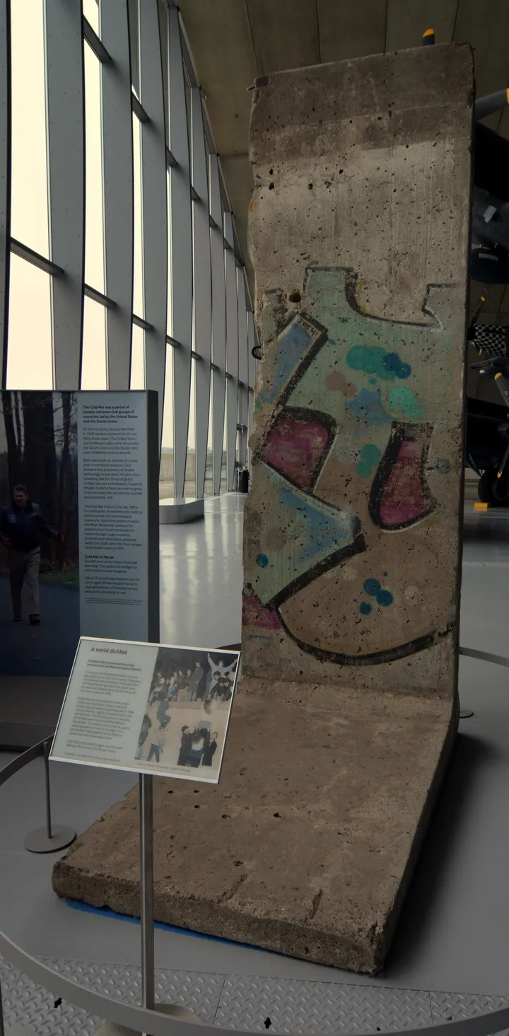 A painted section of the Berlin Wall standing inside an aircraft hangar.