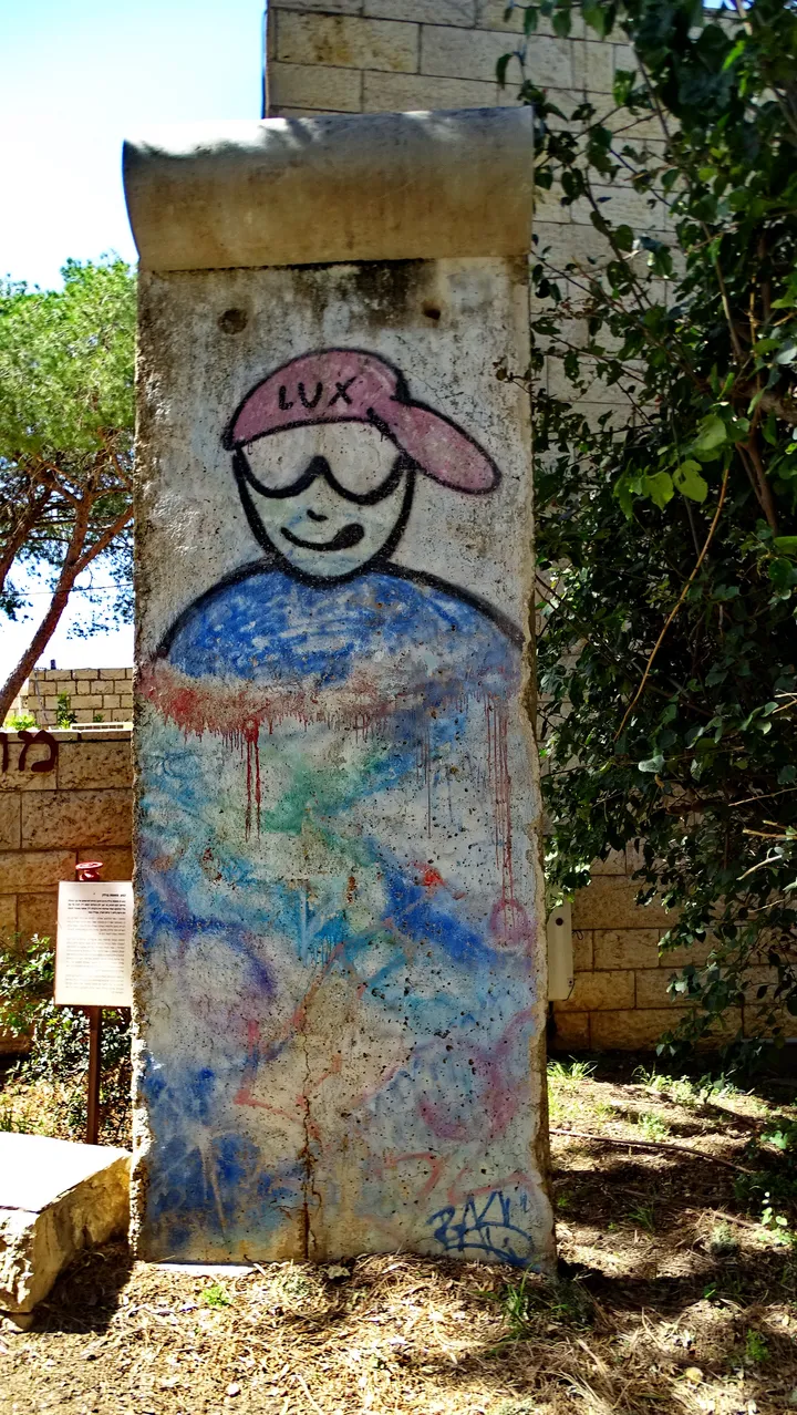 A painted section of the Berlin Wall standing outdoors beside a stone building.