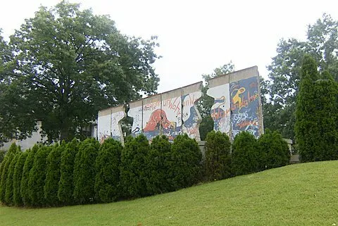A row of painted Berlin Wall segments with human silhouettes cut through the concrete.
