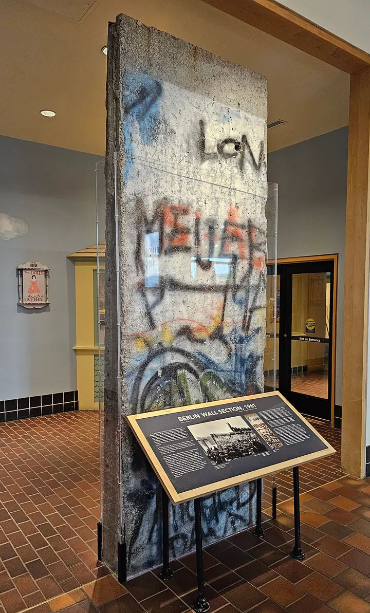 A painted Berlin Wall section standing indoors on a museum floor beside an information panel.