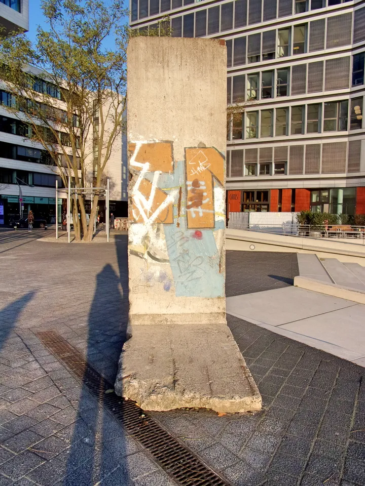 A painted Berlin Wall segment standing on a paved square in front of modern buildings.
