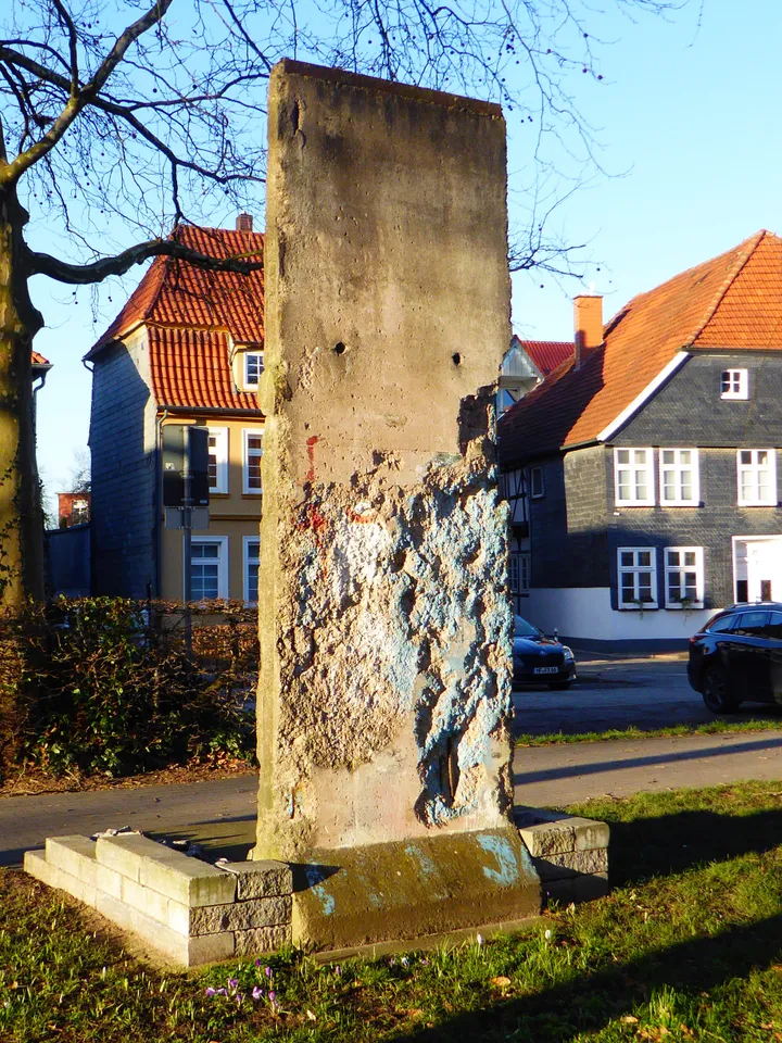 A painted Berlin Wall element standing outdoors beside a path.