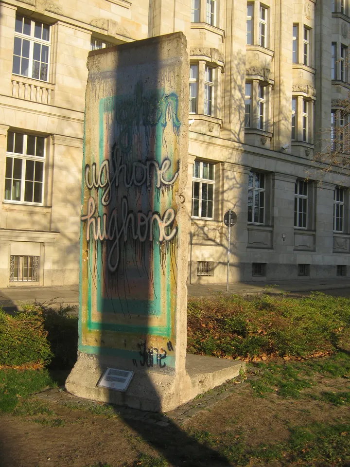 A painted Berlin Wall segment standing on a paved area beside a city ring road.