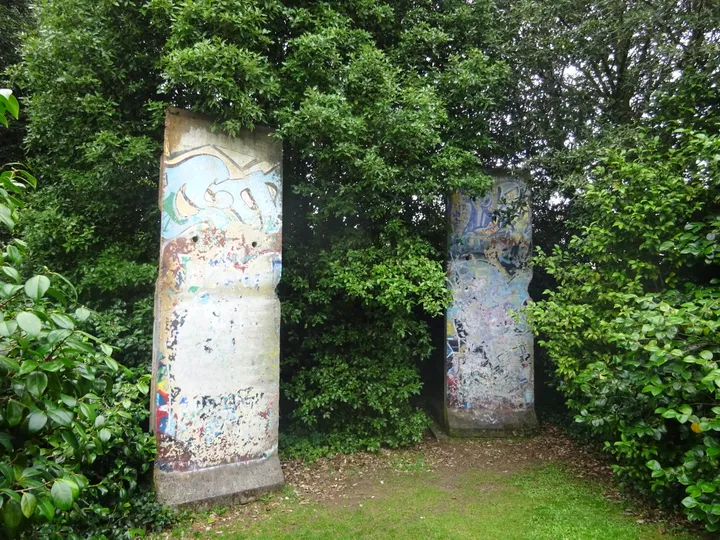 Two painted Berlin Wall segments standing on grass in a walled garden.