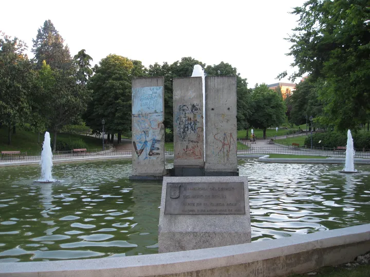 Painted Berlin Wall segments standing beside a pond in a city park.