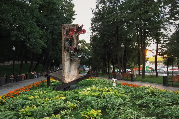 A painted fragment of the Berlin Wall mounted on a low base in a small urban park.