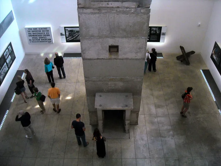 A three-storey concrete guard tower standing indoors beside sections of the Berlin Wall.
