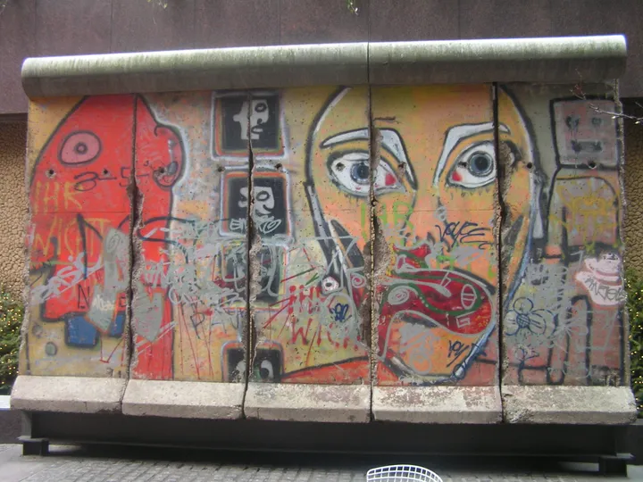 Painted Berlin Wall panels standing in a small paved urban park.