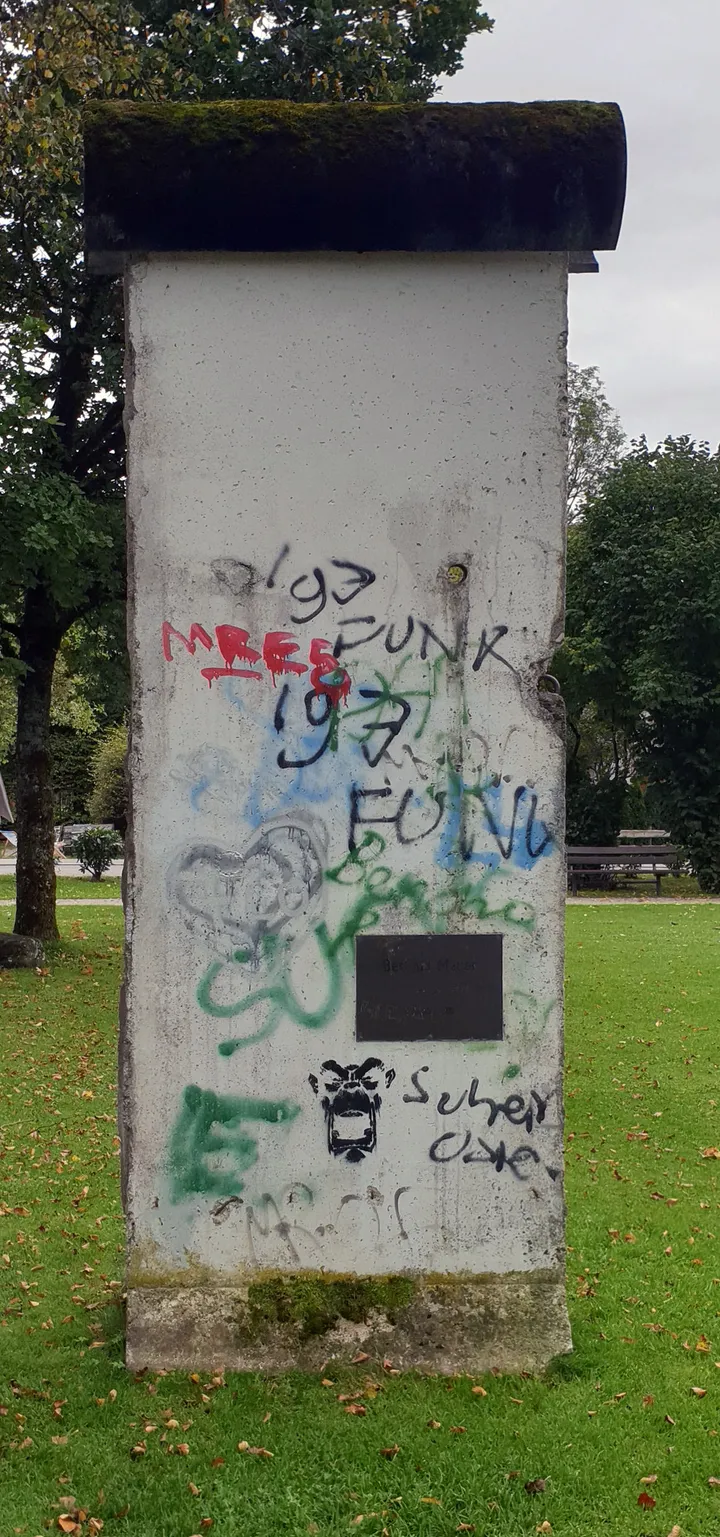A memorial stone beside a piece of the Berlin Wall in a park.