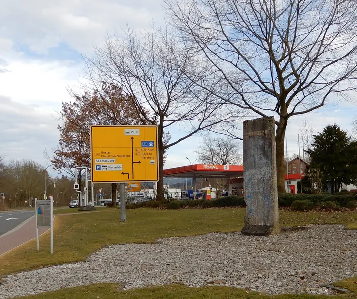 A Berlin Wall memorial standing at a roadside in a wooded setting.