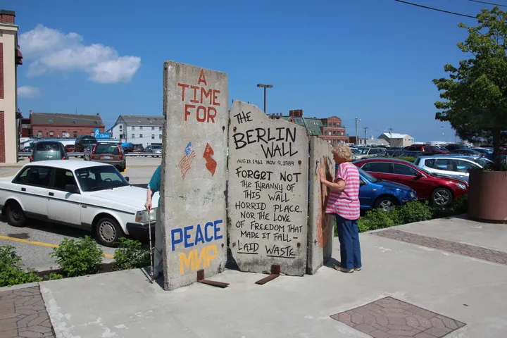 Painted Berlin Wall segments standing on a paved waterfront wharf.