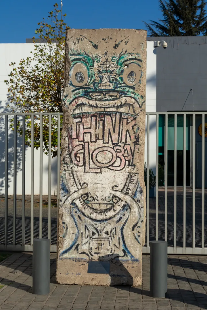 A painted Berlin Wall segment standing outdoors behind a low fence.