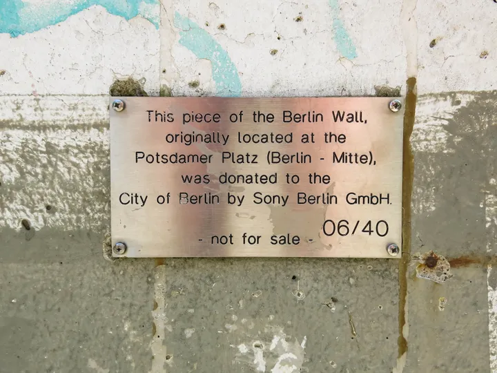 A painted Berlin Wall segment standing on grass beside a riverside path.