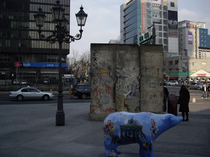Three Berlin Wall sections with a Berlin street lamp beside a paved stream-side walkway.