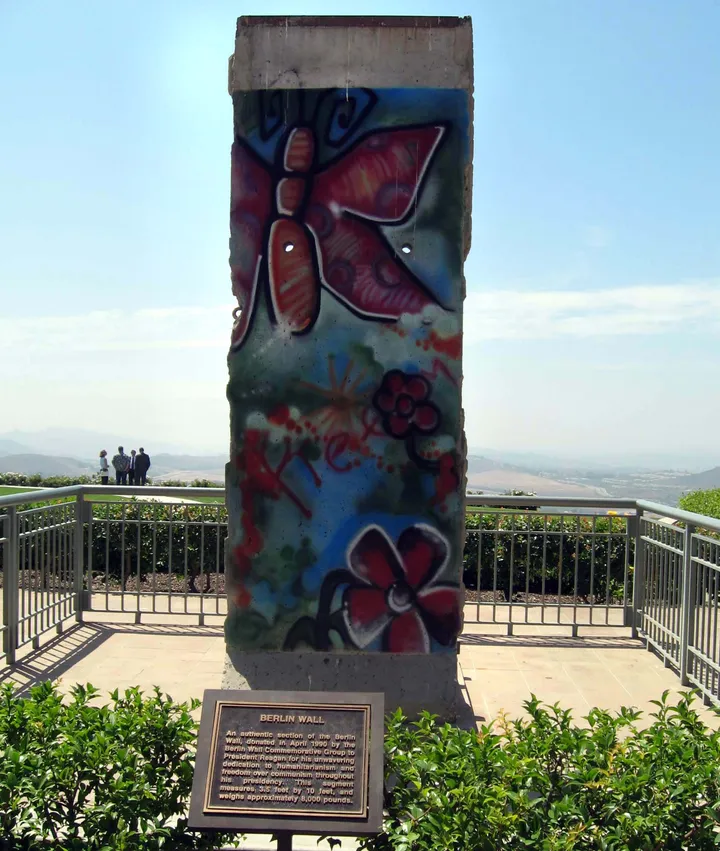 A painted Berlin Wall panel standing on a plinth outside a low building.