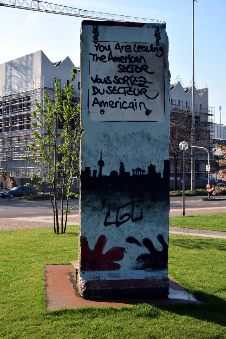 A painted Berlin Wall segment standing on grass in a park beside a modern parliament building.