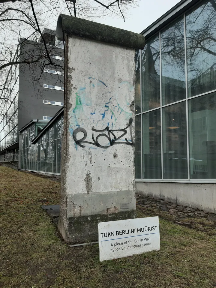 A concrete Berlin Wall segment standing outdoors beside a museum building.