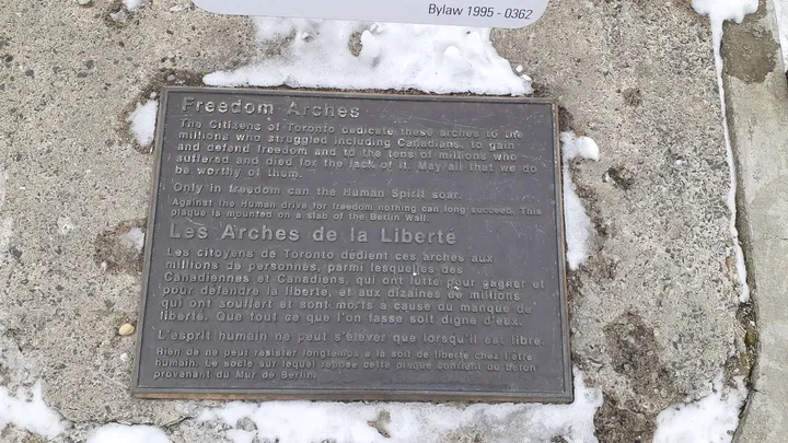 A bronze plaque mounted at the base of a concrete arch in a city square.